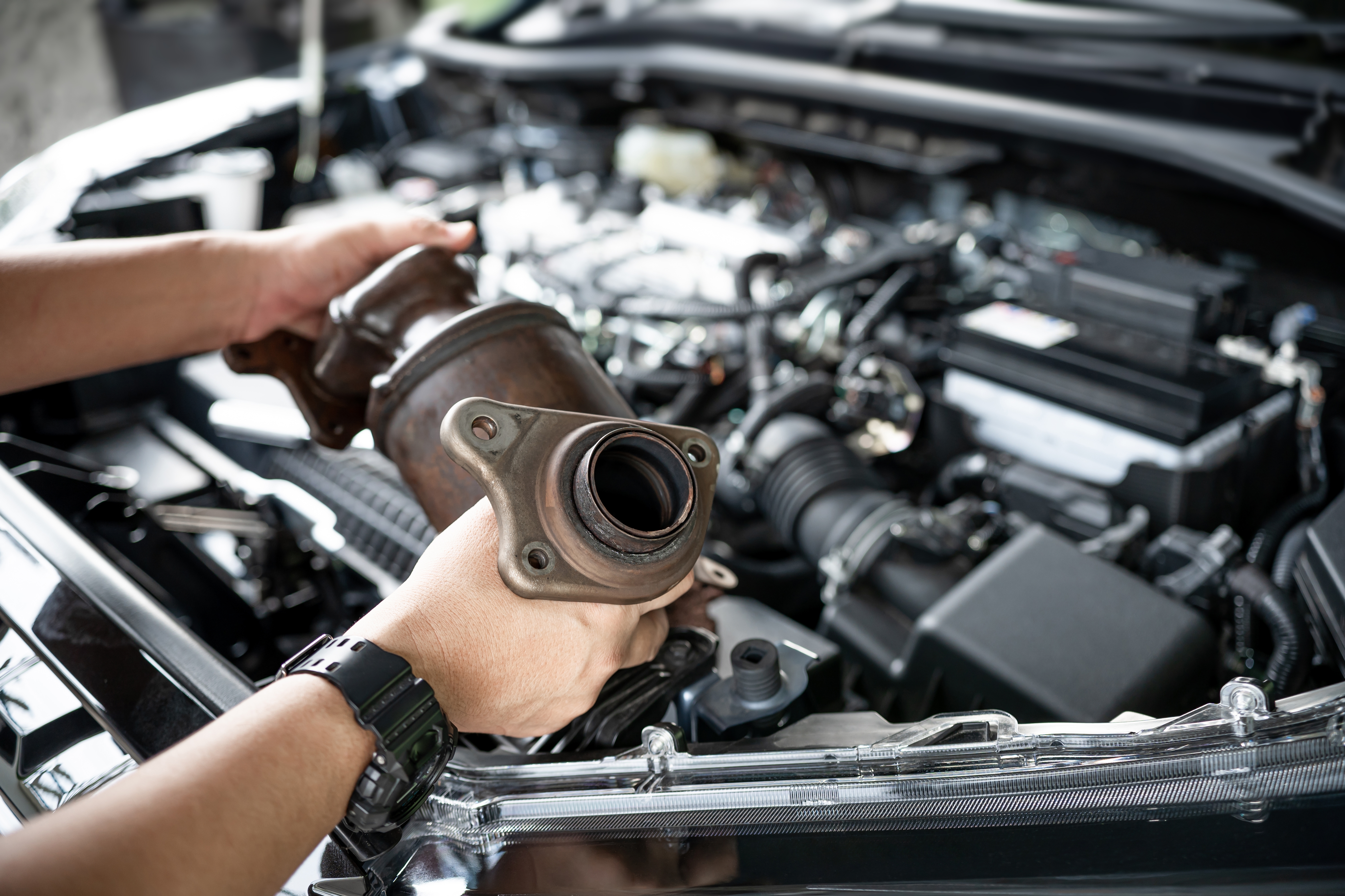 Man-removing-old-catalytic-converter-from-car-engine